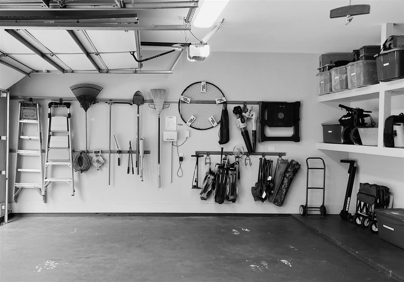 A garage wall with rails holding tools, golf bags and gear in tidy rows