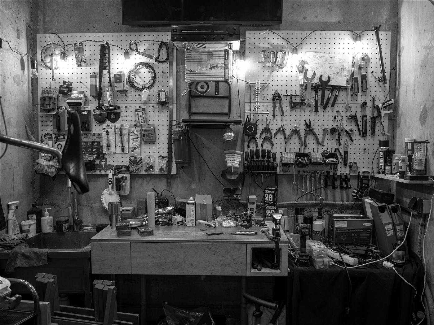 A workbench buried under tools and parts with a crowded pegboard